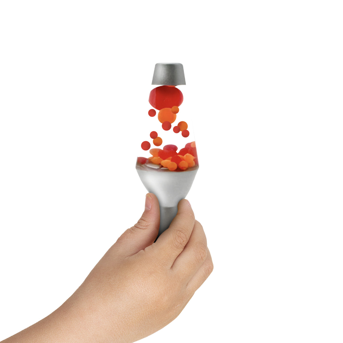 A hand holding a small, squishy silver Lamp toy. Red and orange globs float upward from the base, giving the illusion of the lamp's typical flowing motion against a plain white background.